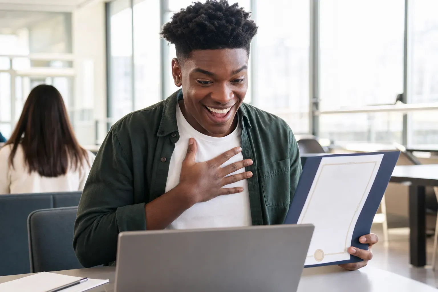 A joyful student receiving a scholarship award letter on a laptop in a bright classroom